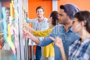 Smiling executives reading sticky notes on glass wall