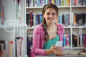 Smiling schoolgirl using mobile phone in library at school