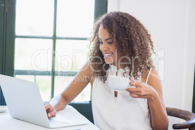 Woman holding coffee cup and using laptop in a restaurant