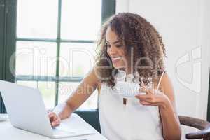 Woman holding coffee cup and using laptop in a restaurant