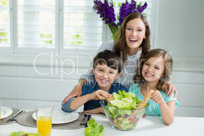 Smiling mother and childrens mixing bowl of salad in kitchen