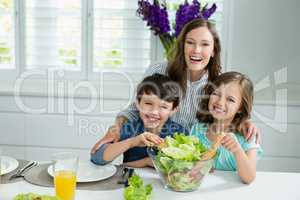 Smiling mother and childrens mixing bowl of salad in kitchen
