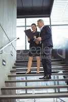 Business executives discussing over clipboard on stairs