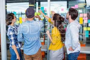 Executives discussing over sticky notes on glass wall