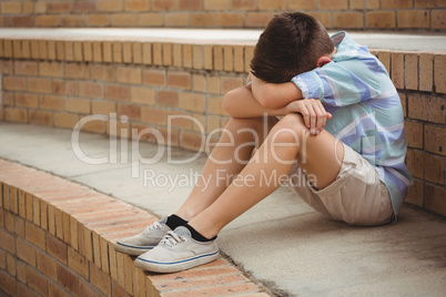 Sad schoolboy sitting alone on steps in campus