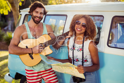 Man playing guitar near campervan and woman holding map beside him