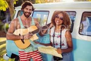 Man playing guitar near campervan and woman holding map beside him