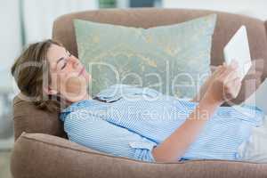 Woman using digital tablet while lying on sofa in living room