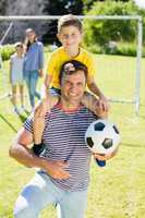 Smiling father with football carrying his son on shoulder at the park