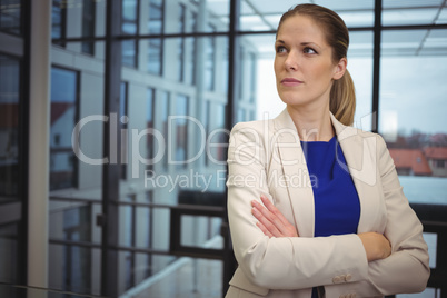 Thoughtful businesswoman standing with arms crossed in corridor