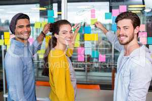 Smiling executives writing on sticky note on glass wall in office