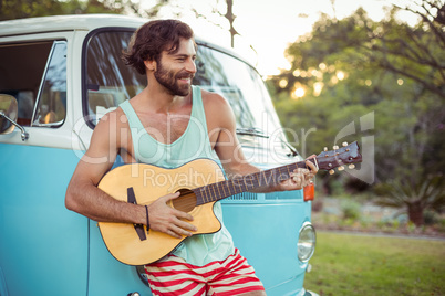 Man playing guitar in front of campervan at campsite