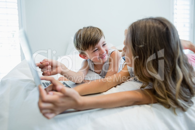 Girl and boy using laptop on bed in bedroom at home