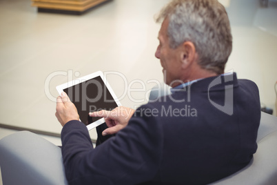 Attentive businessman sitting on sofa and using digital tablet