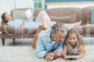 Happy father and daughter using mobile phone while lying on floor in living room