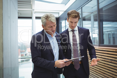 Businesspeople discussing over clipboard in the corridor