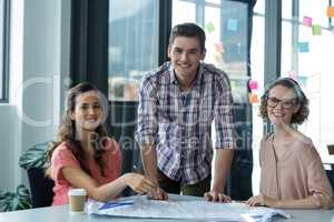 Portrait of smiling business executives with blueprint on table