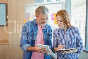 Male executive using digital tablet while female executive writing on diary