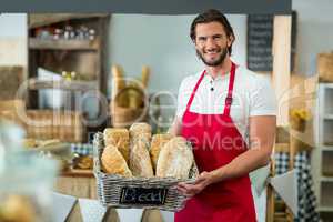 Portrait of smiling male staff holding a basket of baguettes at counter