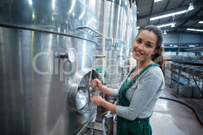 Female factory worker turning control wheel of storage tank