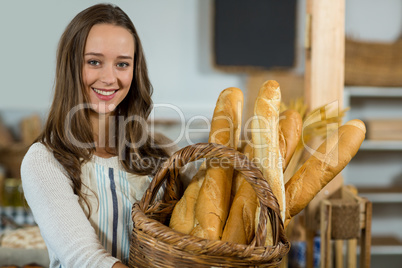 Portrait of smiling female staff holding a basket of baguettes at counter