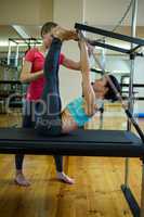Female trainer assisting woman with stretching exercise on reformer