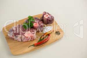 Sirloin chops, salt and chillies on wooden board against white background