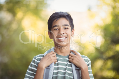 Smiling schoolboy standing with schoolbag in campus