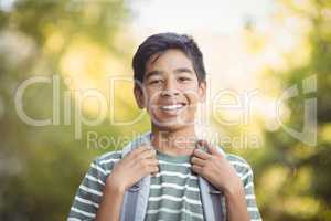 Smiling schoolboy standing with schoolbag in campus