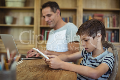 Father and son using laptop and digital tablet in study room