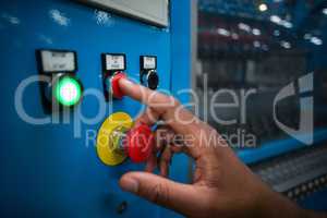 Hands of factory worker pressing a red button on the control board