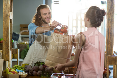 Vendor handing a bag of vegetables to woman at grocery store