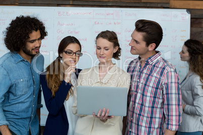 Business team discussing over laptop while colleague working in background