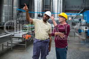 Two factory workers pointing upwards while discussing together