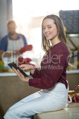 Portrait of smiling female staff sitting at counter using digital tablet