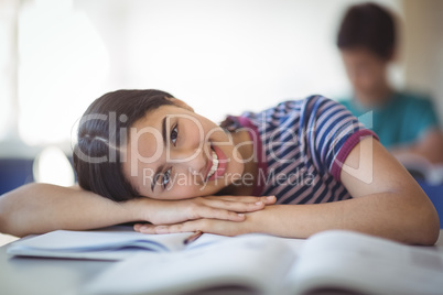 Portrait of happy schoolgirl leaning on bench in classroom