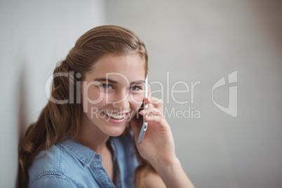 Portrait of happy schoolgirl talking on mobile phone in corridor