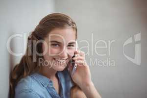 Portrait of happy schoolgirl talking on mobile phone in corridor