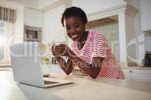 Portrait of woman using laptop while having coffee in kitchen