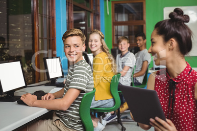 Smiling students studying on digital tablet and computer in classroom