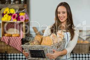 Portrait of smiling female staff holding a basket of baguettes at counter