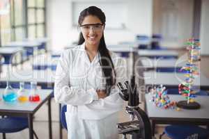 Portrait of schoolgirl in lab coat standing with arms crossed in laboratory