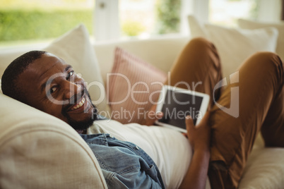 Man lying on sofa and using digital tablet