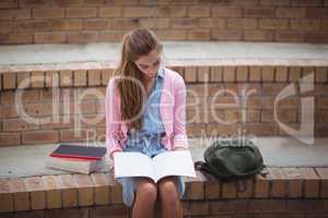 Attentive schoolgirl reading book in campus