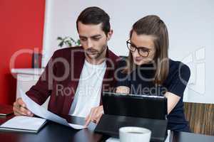 Two business executives discussing over digital tablet and document in meeting