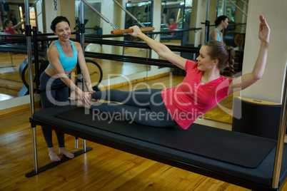 Female trainer assisting woman with stretching exercise on reformer