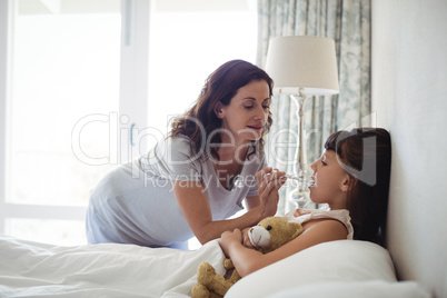 Mother checking temperature of sick daughter lying on bed
