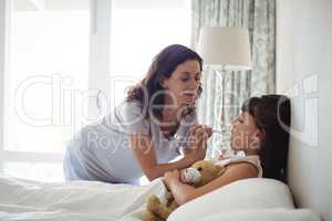 Mother checking temperature of sick daughter lying on bed