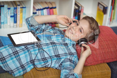 Schoolboy relaxing on couch while listening music on digital tablet in library