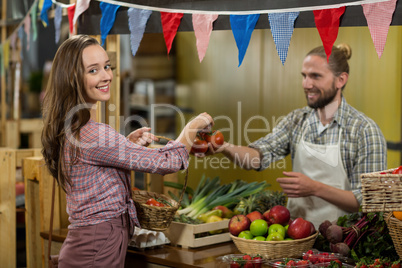 Smiling vendor giving tomatoes to woman at the counter in the grocery store